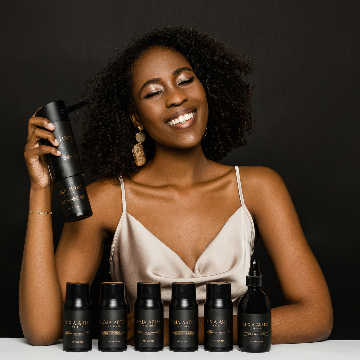 Model smiling with Luxia Artiss Keratin Thickening Fibers, the Precision Control Applicator and Set &amp; Seal Spray